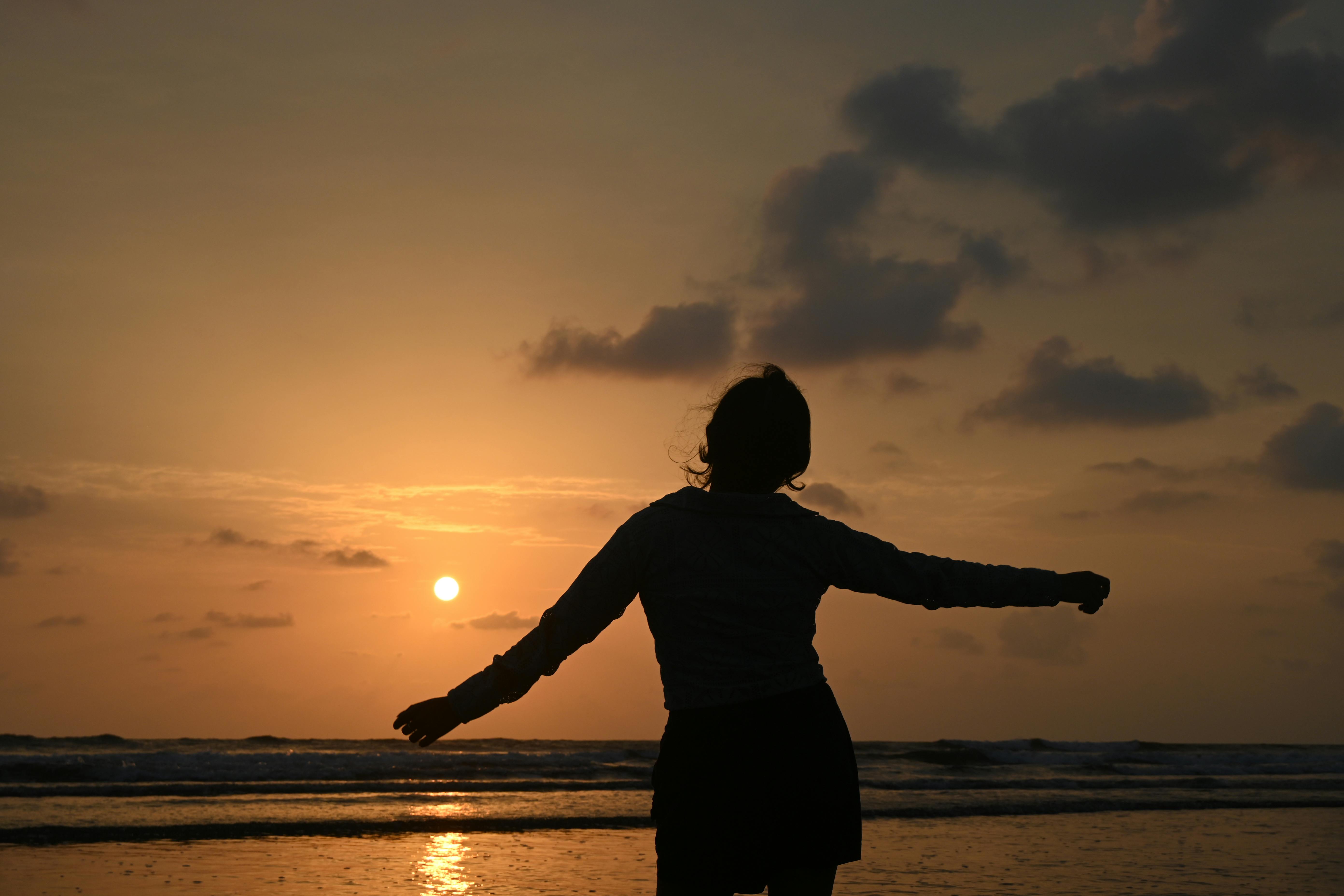 A woman enjoys the Sunset at Murud Beach, India, casting a serene silhouette against the horizon.