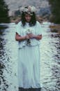 一位身着飘逸白裙、头戴花冠的女子，正立于自然的溪流之中