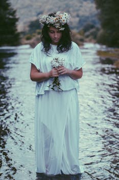 一位身着飘逸白裙、头戴花冠的女子，正立于自然的溪流之中