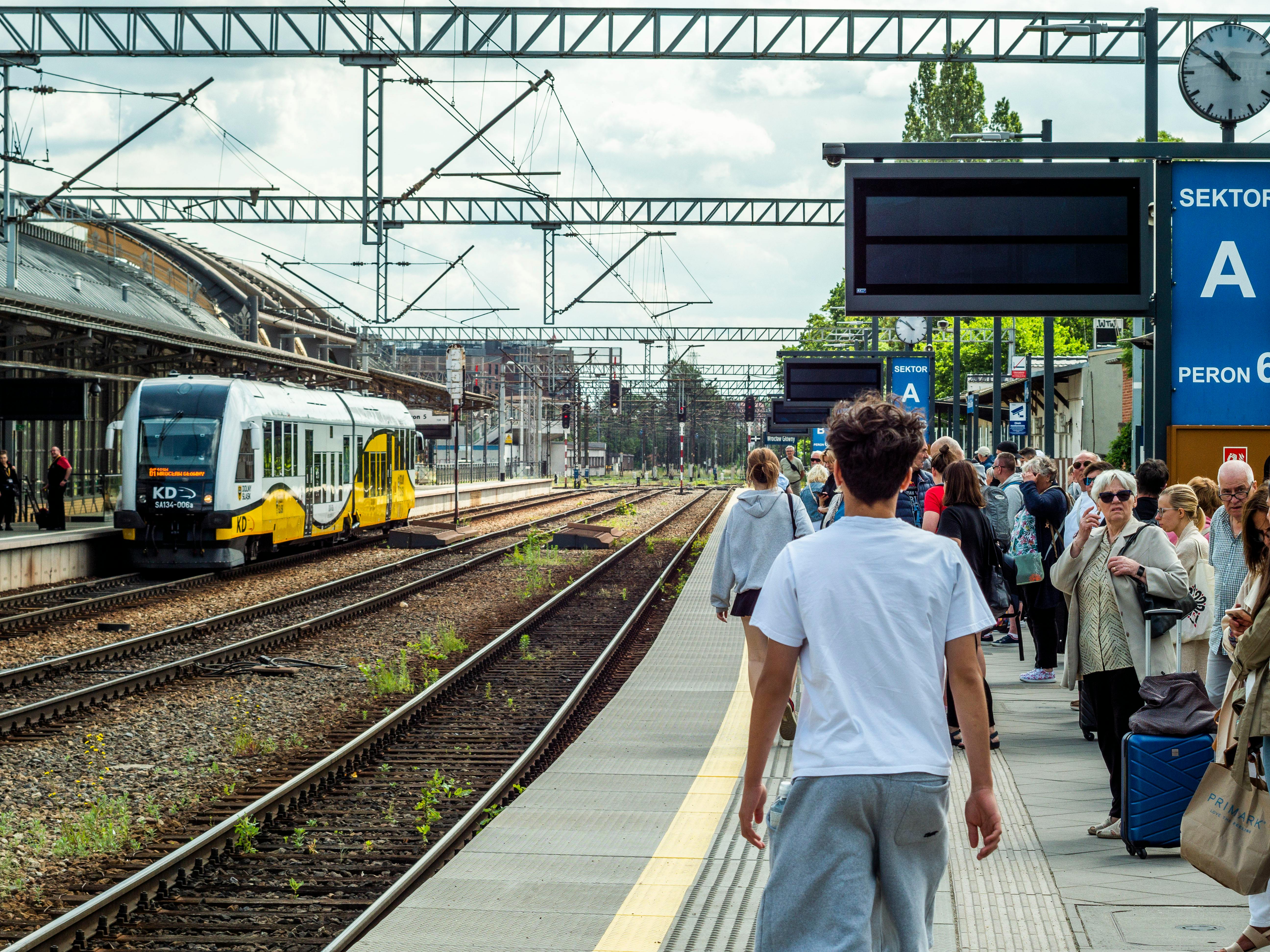 Free Crowd of people waiting for a train at an urban station with tracks and signage. Stock Photo