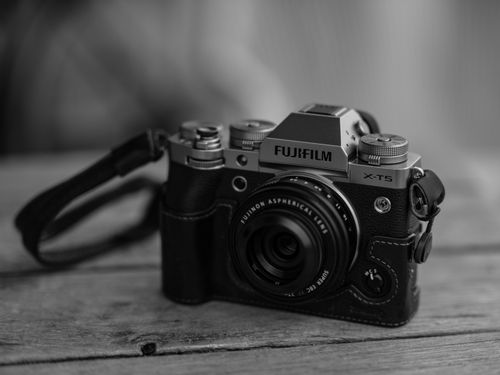 Free A stylish black and white close-up of a Fujifilm X-T5 camera on a wooden surface, showcasing its vintage-modern design. Stock Photo