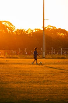 A child in blue soccer gear plays on a field at sunset, creating a warm, serene scene.