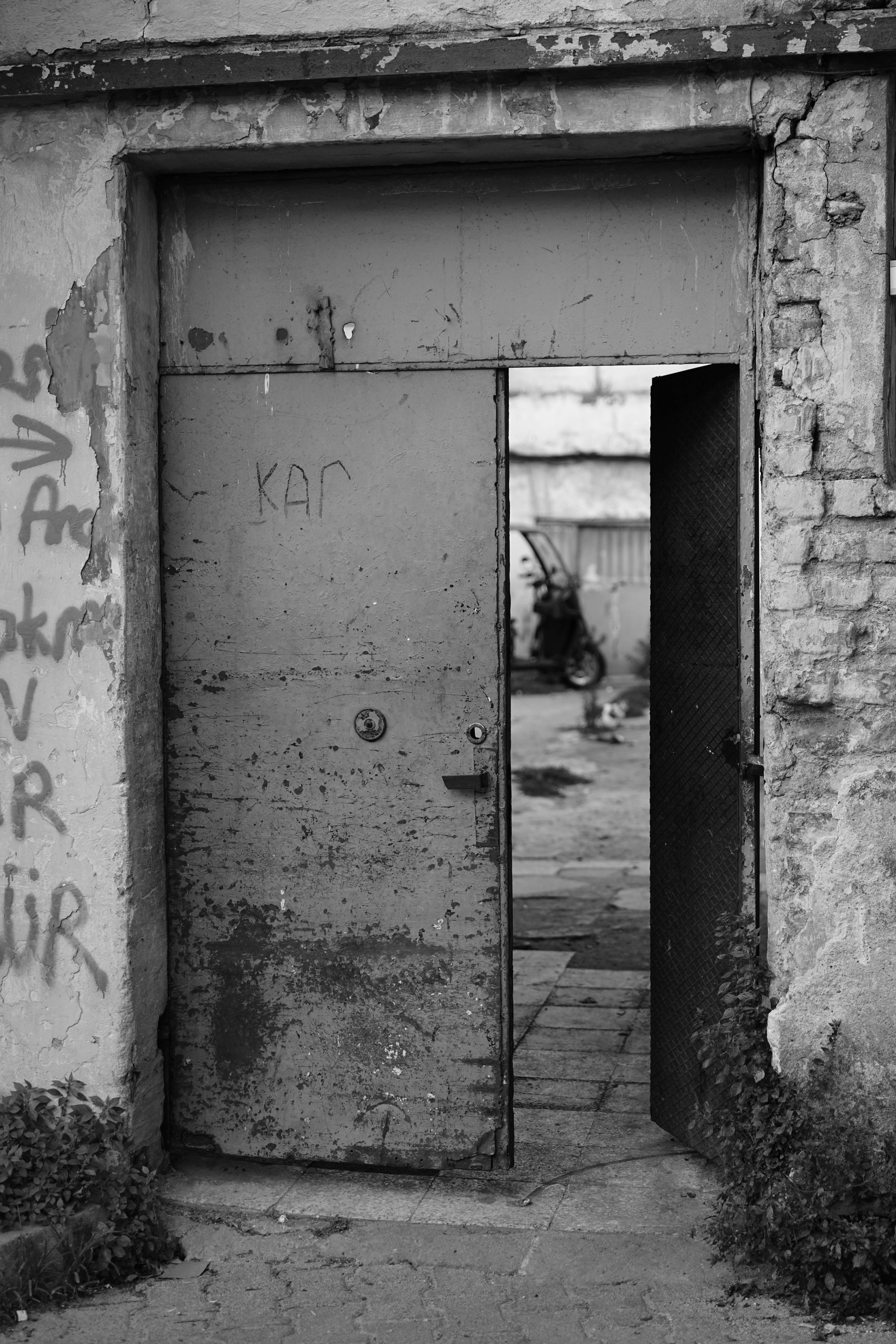 Black and white image of an old metal door showing an urban scene.