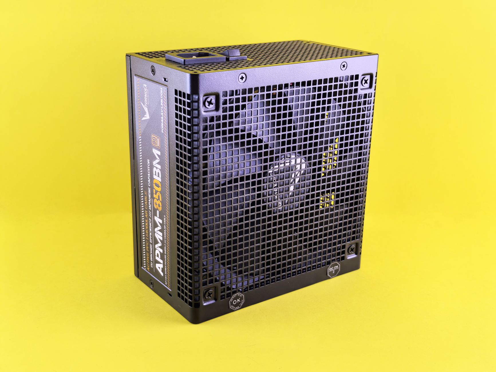 Black computer power supply unit with fan displayed against yellow background.