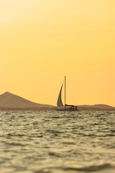 A serene sailboat glides across the Aegean Sea during a stunning sunset near Naxos, Greece.