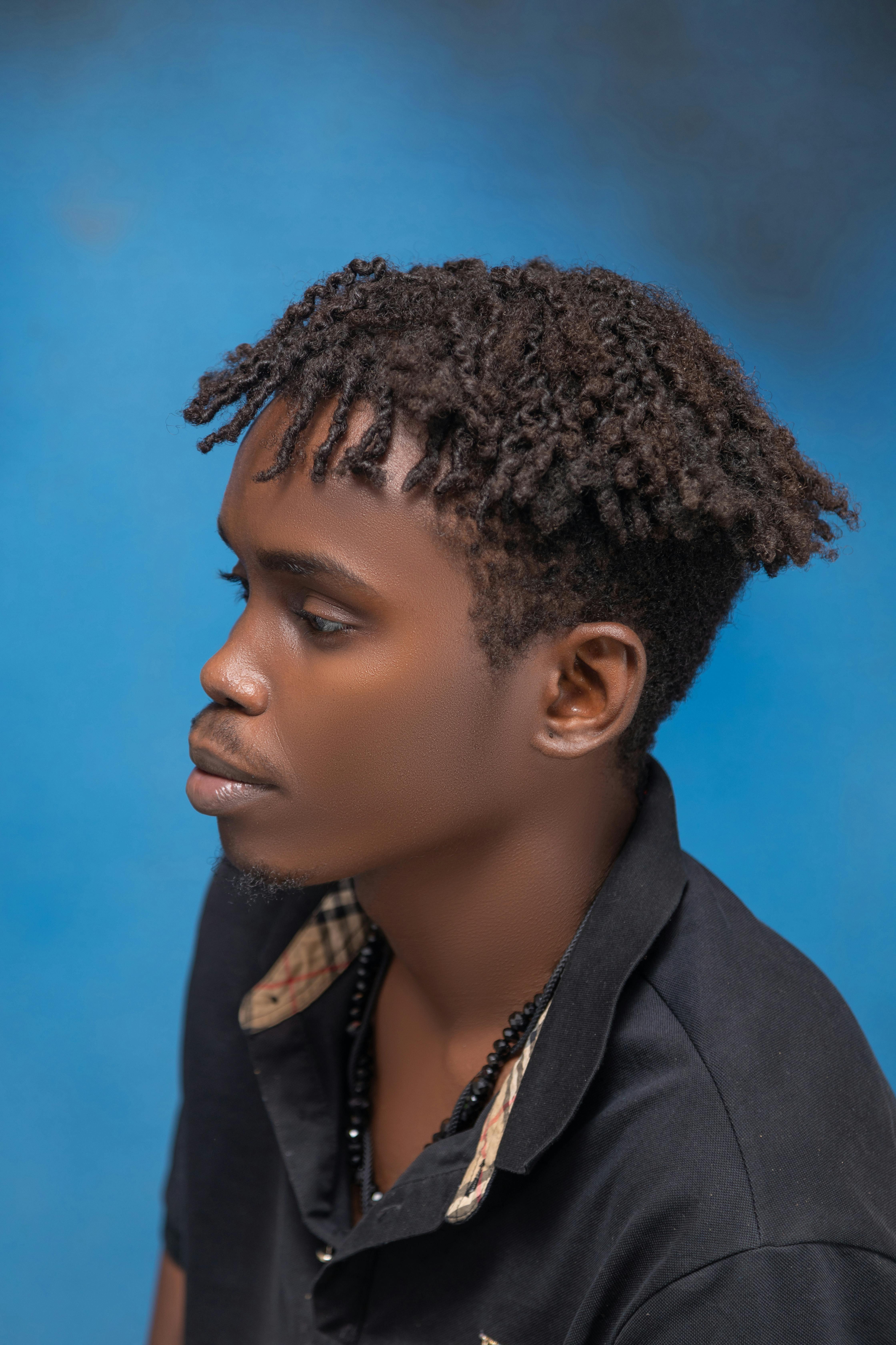 Free Side profile of a young man with curly hair against a blue backdrop, looking serene. Stock Photo