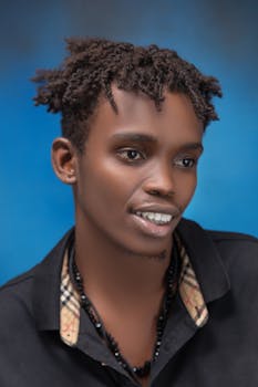 Close-up portrait of a young black male model smiling against a vibrant blue background.