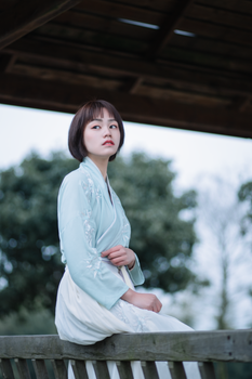 一位身穿传统服装的体贴女子坐在户外，背景是模糊的自然景色