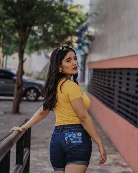 Fashionable woman in casual yellow outfit posing by railing in an urban setting. Shot during the day.