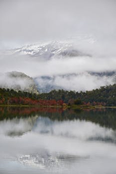 Serene lake reflecting mountains and mist on a fall day.