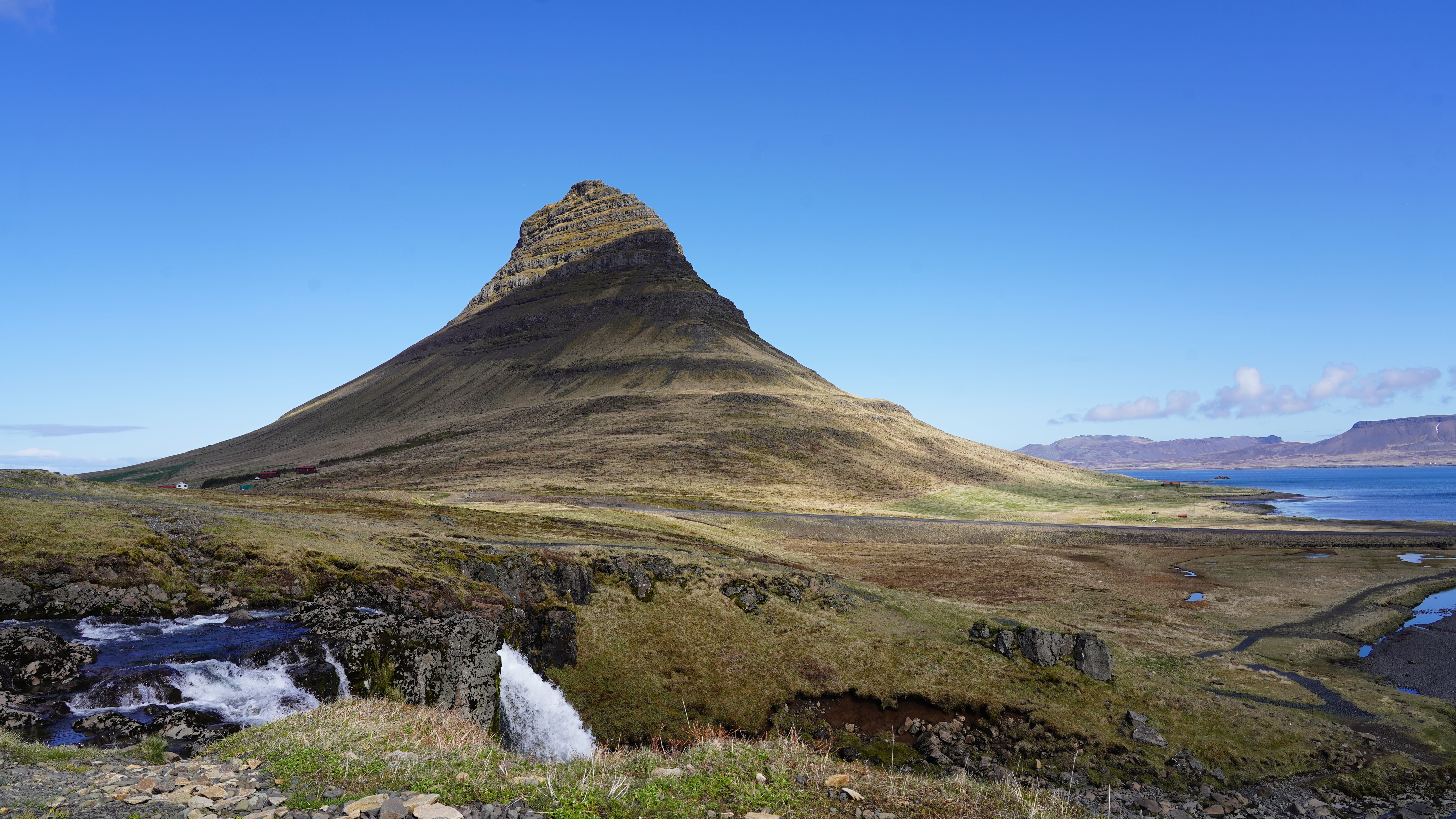Capture of Kirkjufell Mountain in Iceland with blue skies, highlighting its unique shape and natural surroundings. - Snæfellsnes