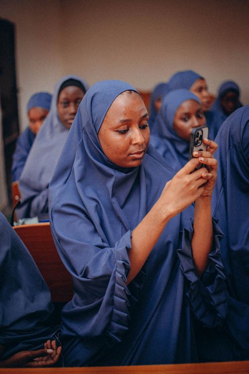 Free Group of women in blue hijabs using smartphones in a classroom setting. Stock Photo