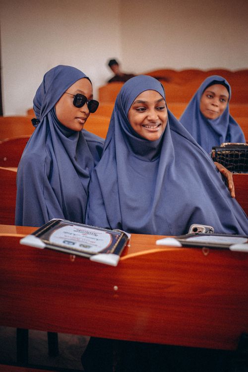 Free Three young women in hijabs smiling while looking at a smartphone in a classroom. Stock Photo