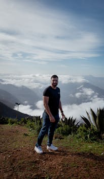 Adult man standing on mountain with breathtaking cloud vista, showcasing nature's beauty.