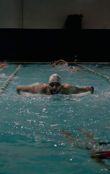 Swimmer executing butterfly stroke in indoor pool, showcasing athletic proficiency and competitive spirit.