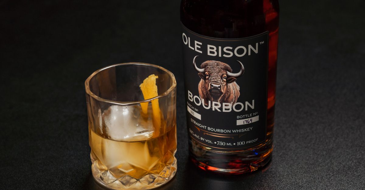 A bottle of Ole Bison Bourbon alongside a glass of whiskey with ice and orange peel.
