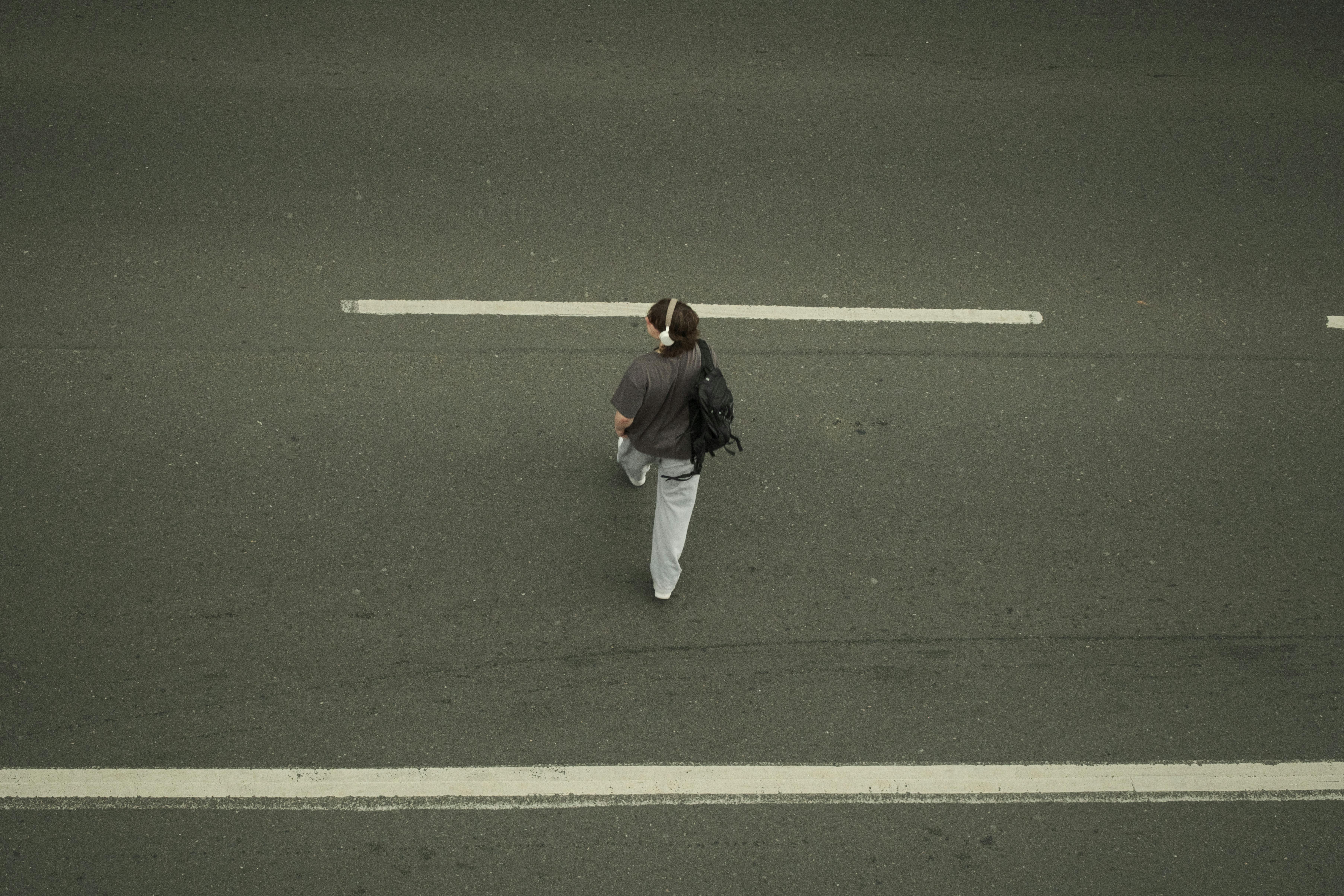 An aerial shot capturing a lone person walking on a city road, emphasizing solitude and travel.