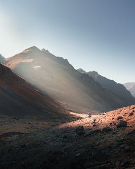 A lone hiker traverses a scenic mountain landscape in Huarochirí, Peru, under the clear day sky.