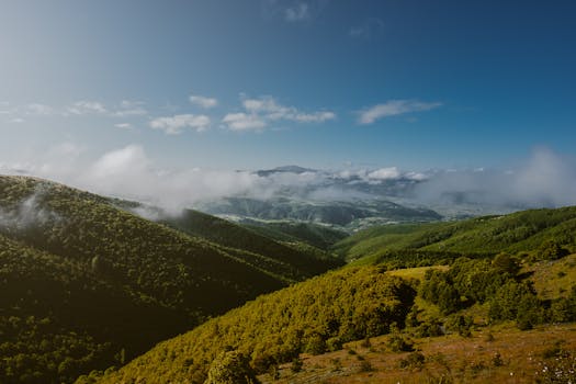 Breathtaking view of lush green mountains under a clear blue sky with rolling clouds.