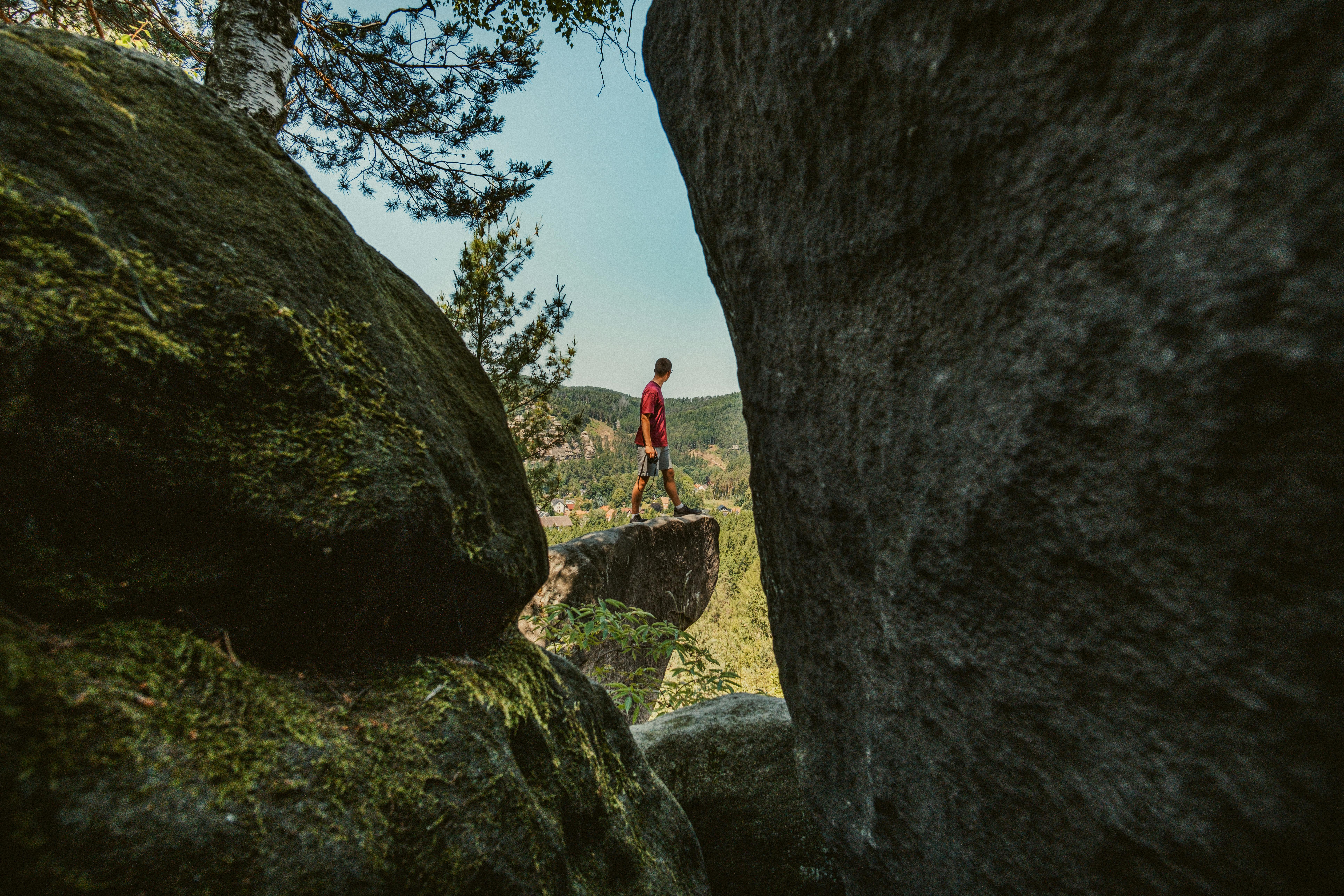 A man stands on a sandstone cliff edge overlooking a scenic forest view in Zittau, Germany.