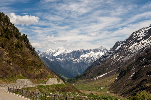 Picturesque view of a mountain road with snow-capped peaks in the Swiss Alps under a bright sky.
