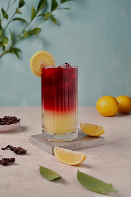 Tall glass of layered lemonade and hibiscus drink garnished with lemon.