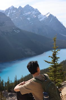 Person sitting with backpack enjoying stunning lake and mountain view in daytime.