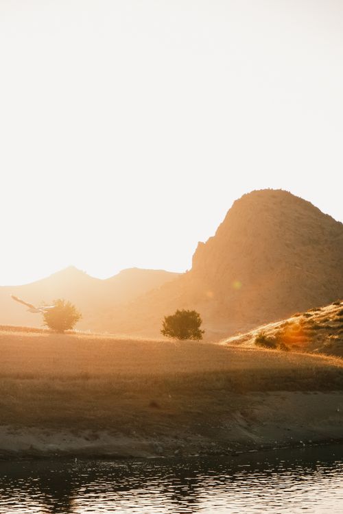 Free A tranquil landscape of rolling hills by a lake during sunset, capturing a serene natural beauty. Stock Photo