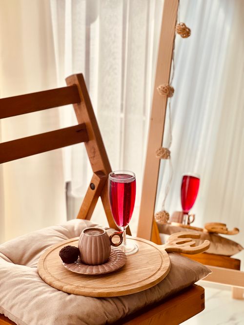 Free A warm, cozy indoor scene featuring a tea set and red beverage on a cushioned wooden chair reflecting in a mirror. Stock Photo