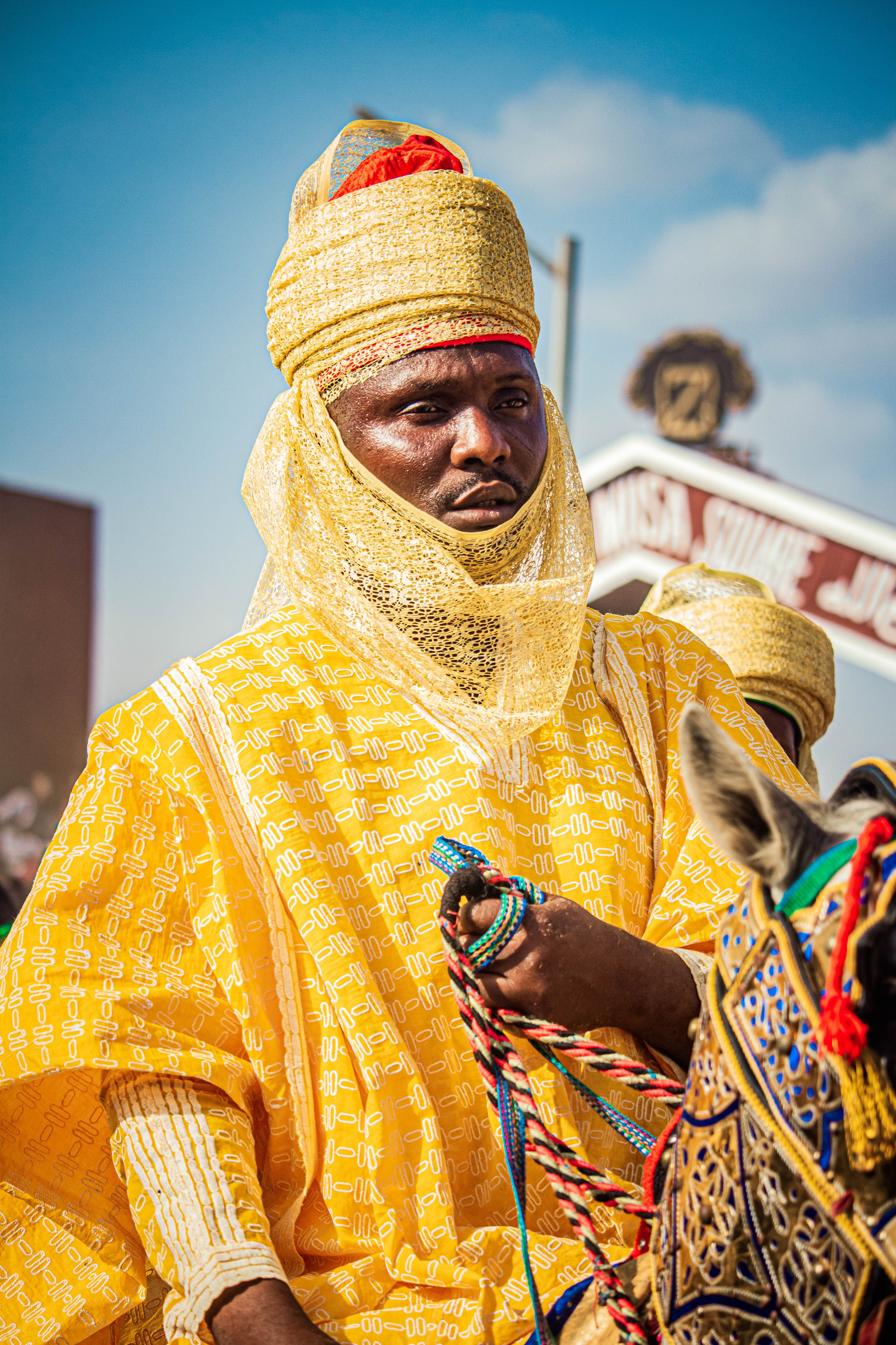 A man in traditional African attire rides a decorated horse in a cultural parade outdoors.