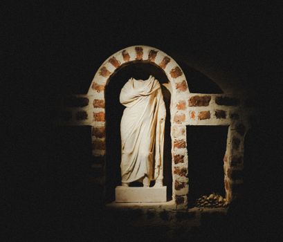 A dimly lit ancient Greek statue in an arched stone niche, capturing historical elegance.