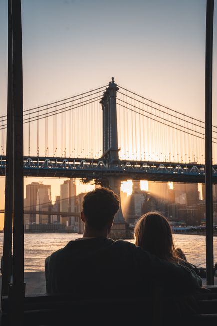 A romantic couple watches the sunset behind the iconic Manhattan Bridge in New York City.