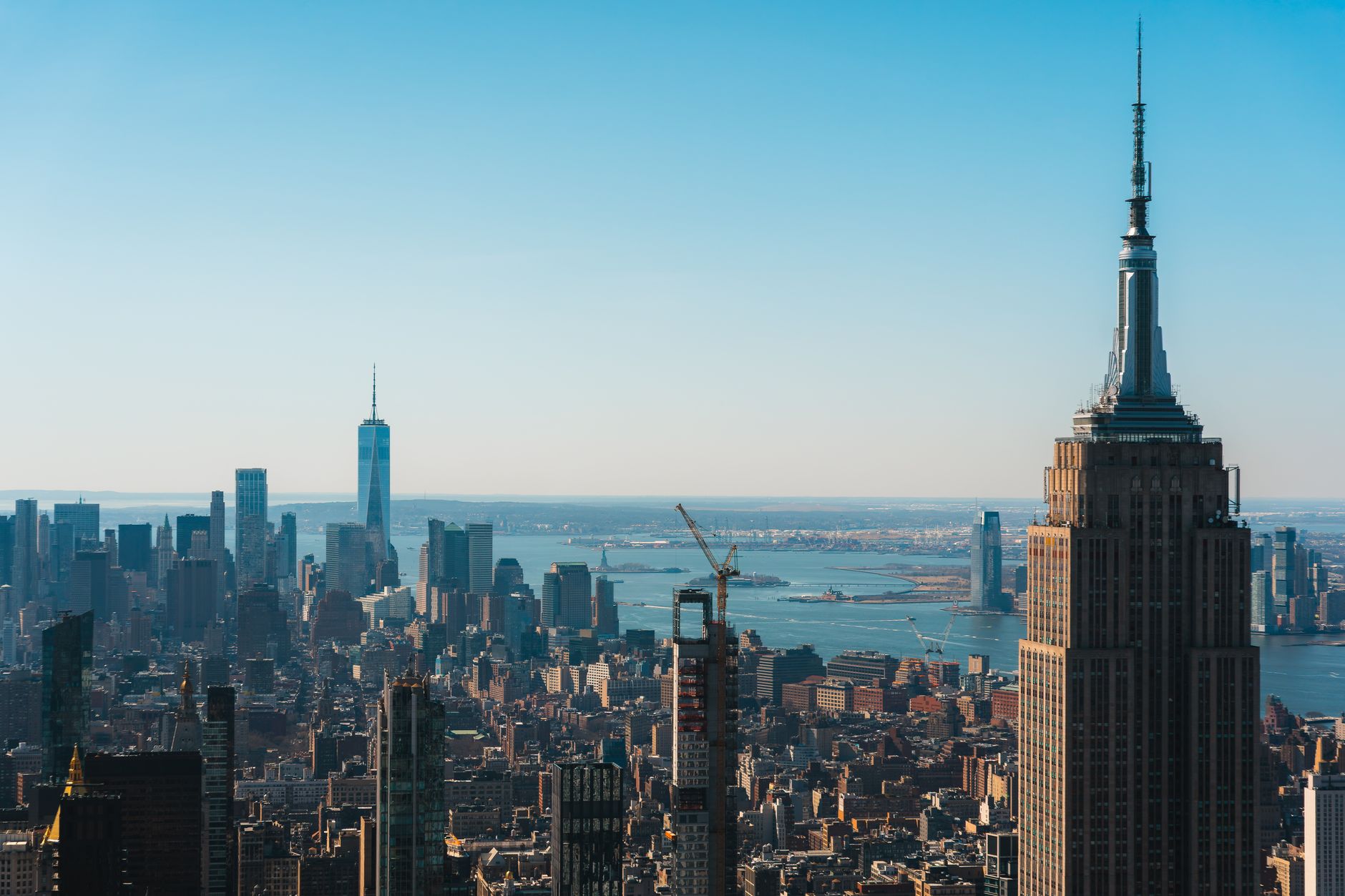 Aerial view of New York City skyline showcasing the Empire State Building and skyscrapers against a clear blue sky.
