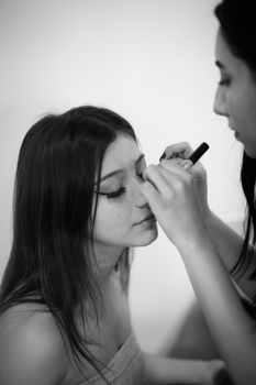 Close-up of makeup artist applying eyeliner to young woman.