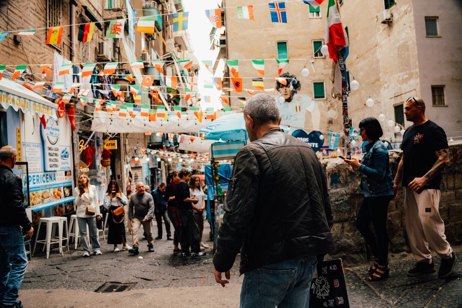 American tourist looking shocked while standing on a crowded street in Naples, Italy, with diverse crowd in background
