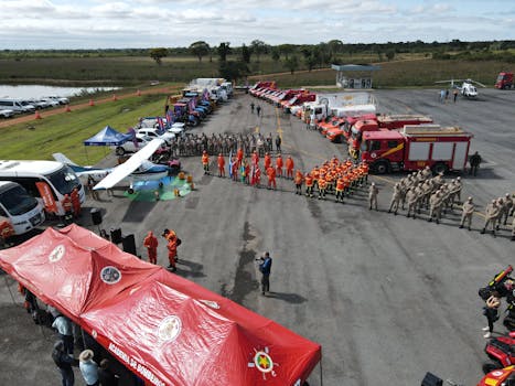 Aerial view of a firefighting team assembly with fire trucks, equipment, and tents outdoors.