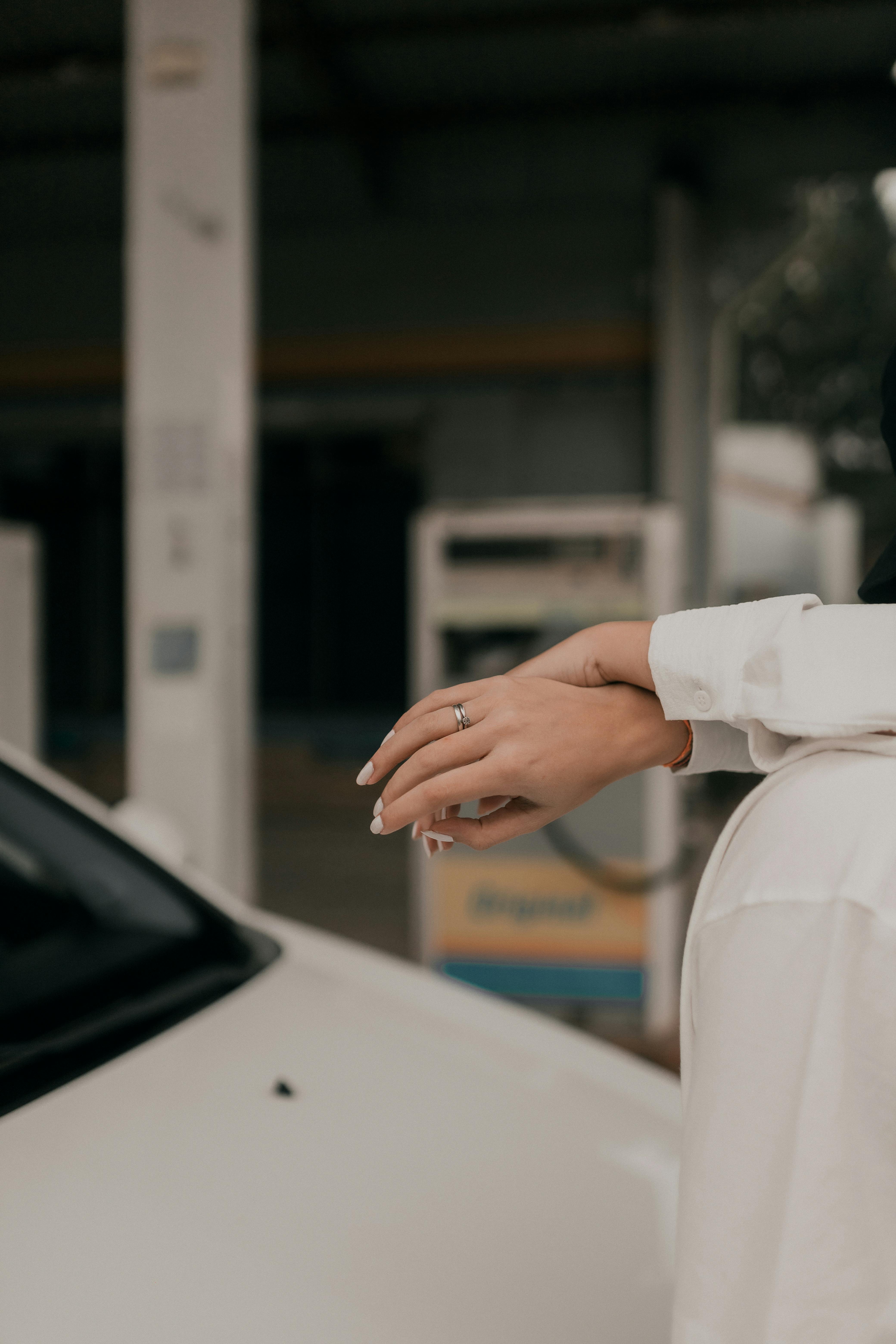 Close-up of a hand with an engagement ring by a white car at a gas station, creating a sophisticated mood.