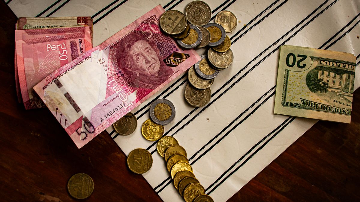 Image of Peruvian banknotes and US dollar bills with scattered coins on a striped surface.