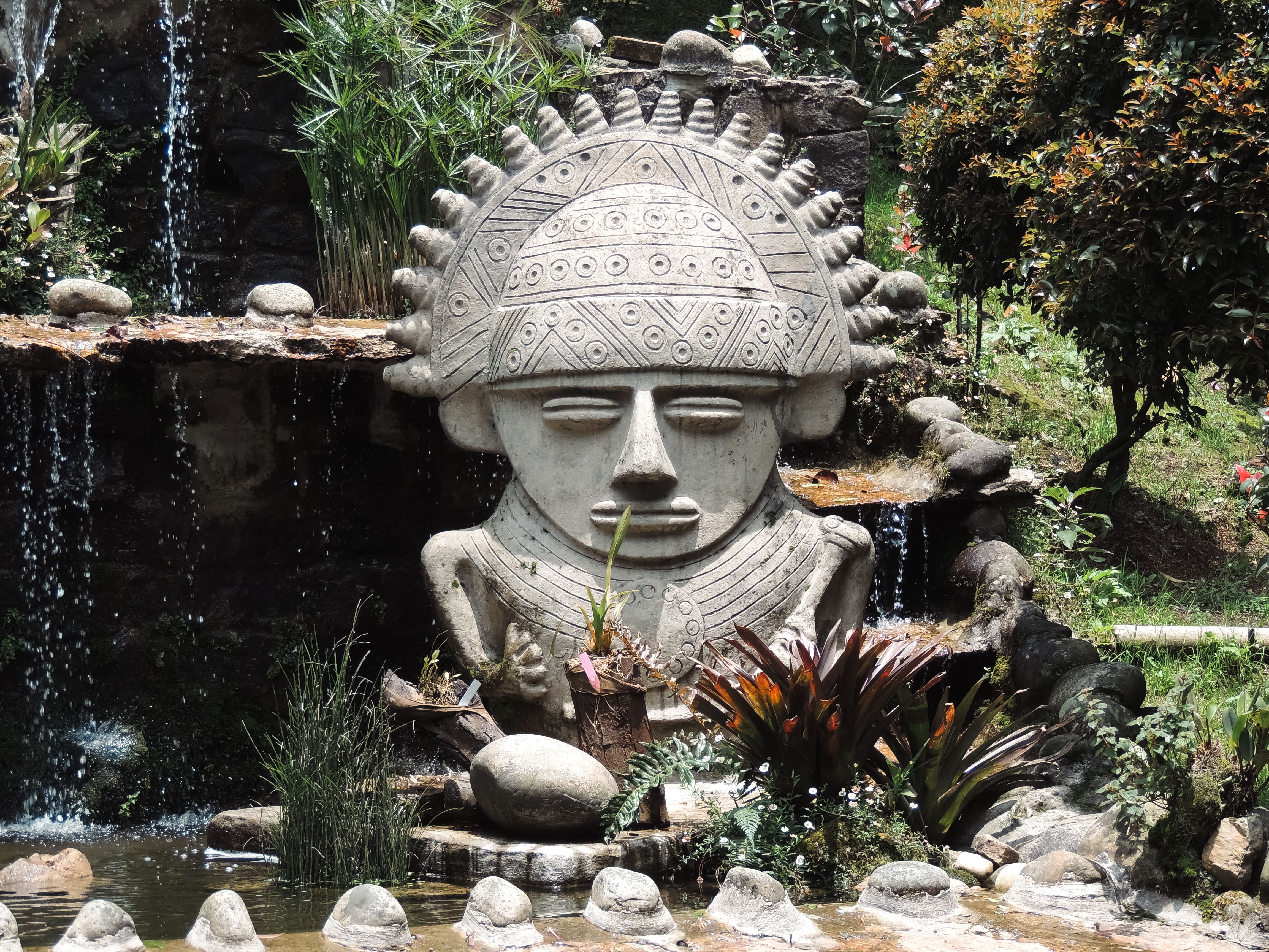 Stone sculpture inspired by Pre-Columbian design in a lush Bogotá garden setting.