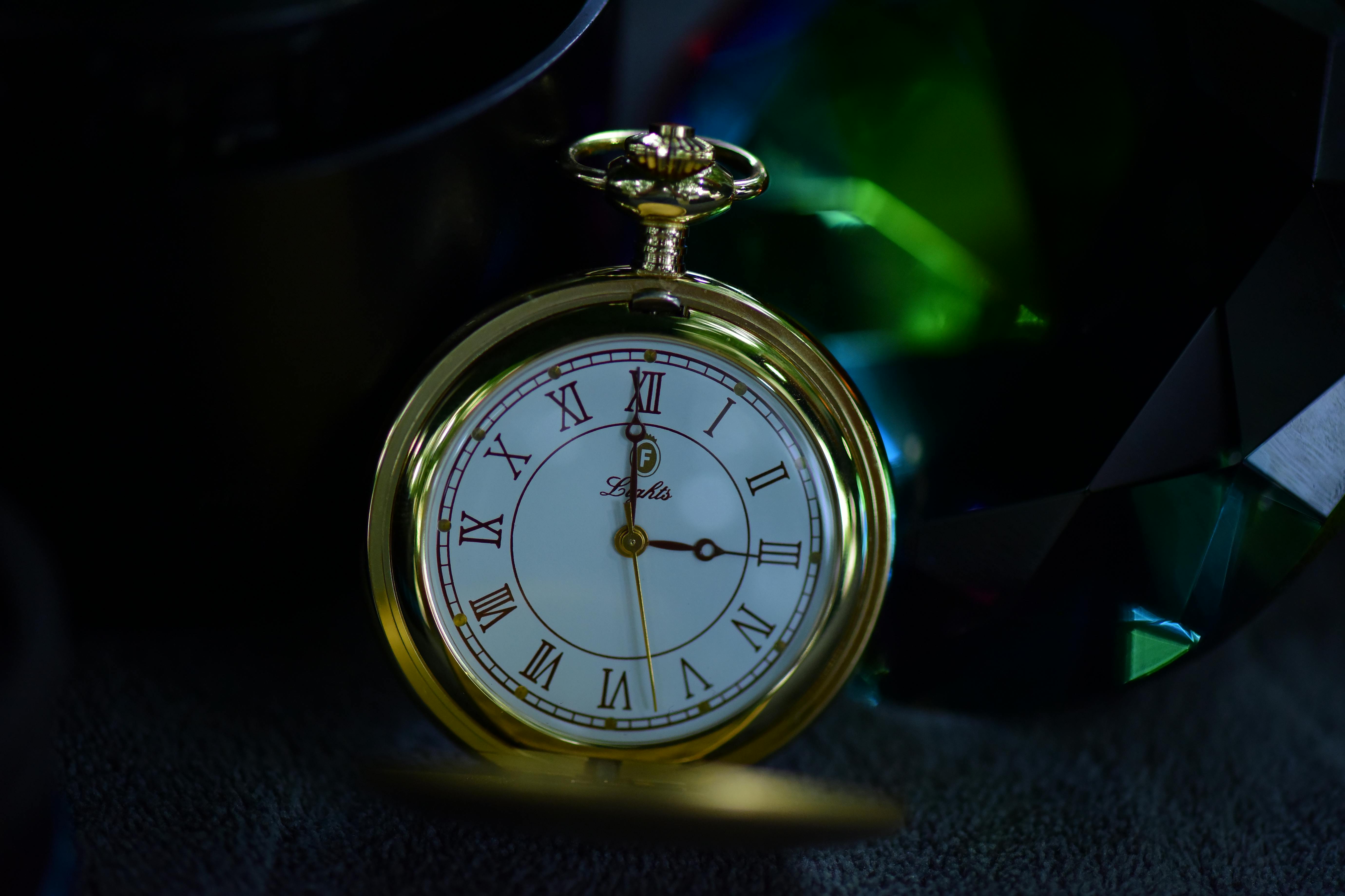 Close-up of a vintage gold pocket watch with Roman numerals on a dark background.