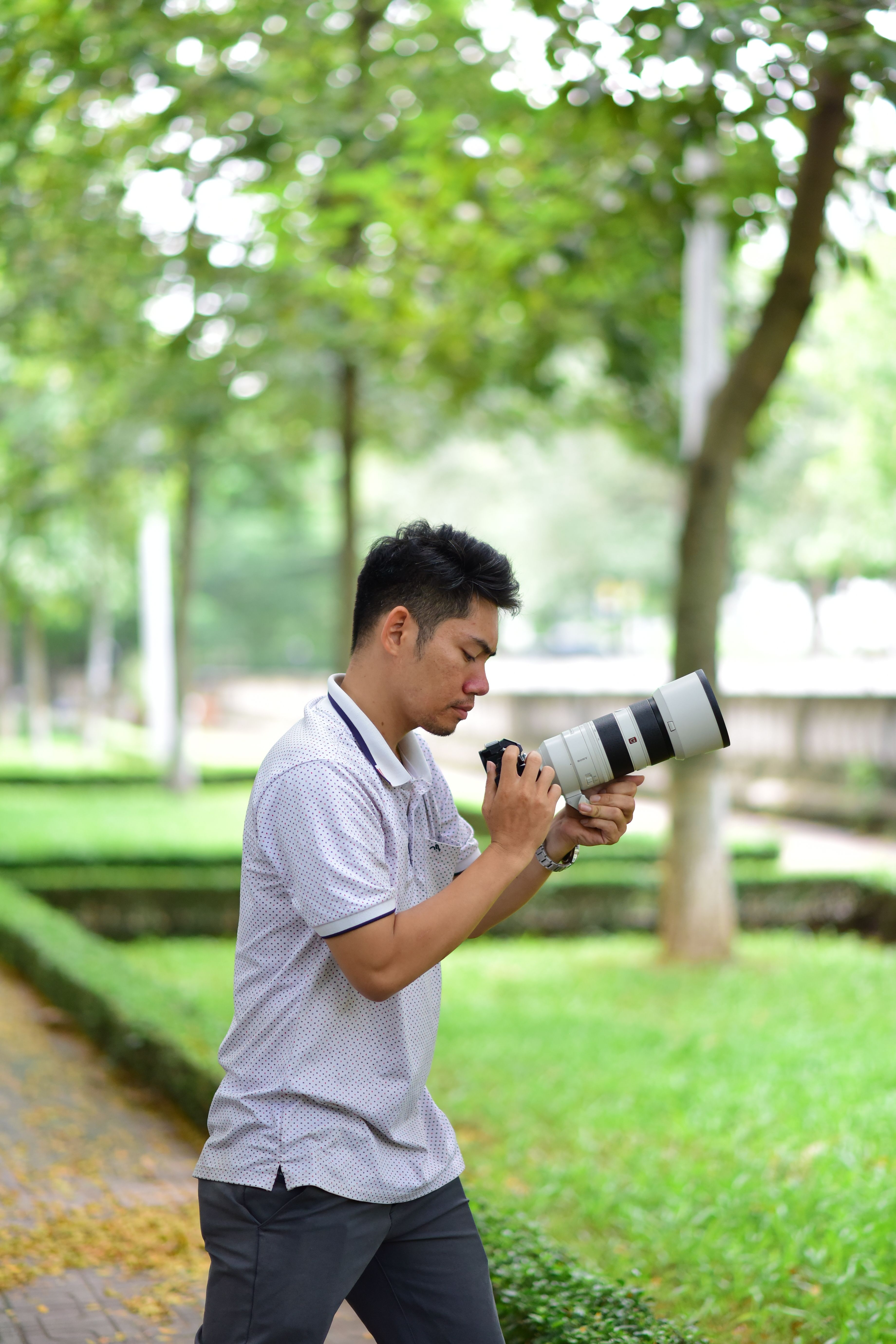 A man with camera and telephoto lens photographing in a green, leafy park.