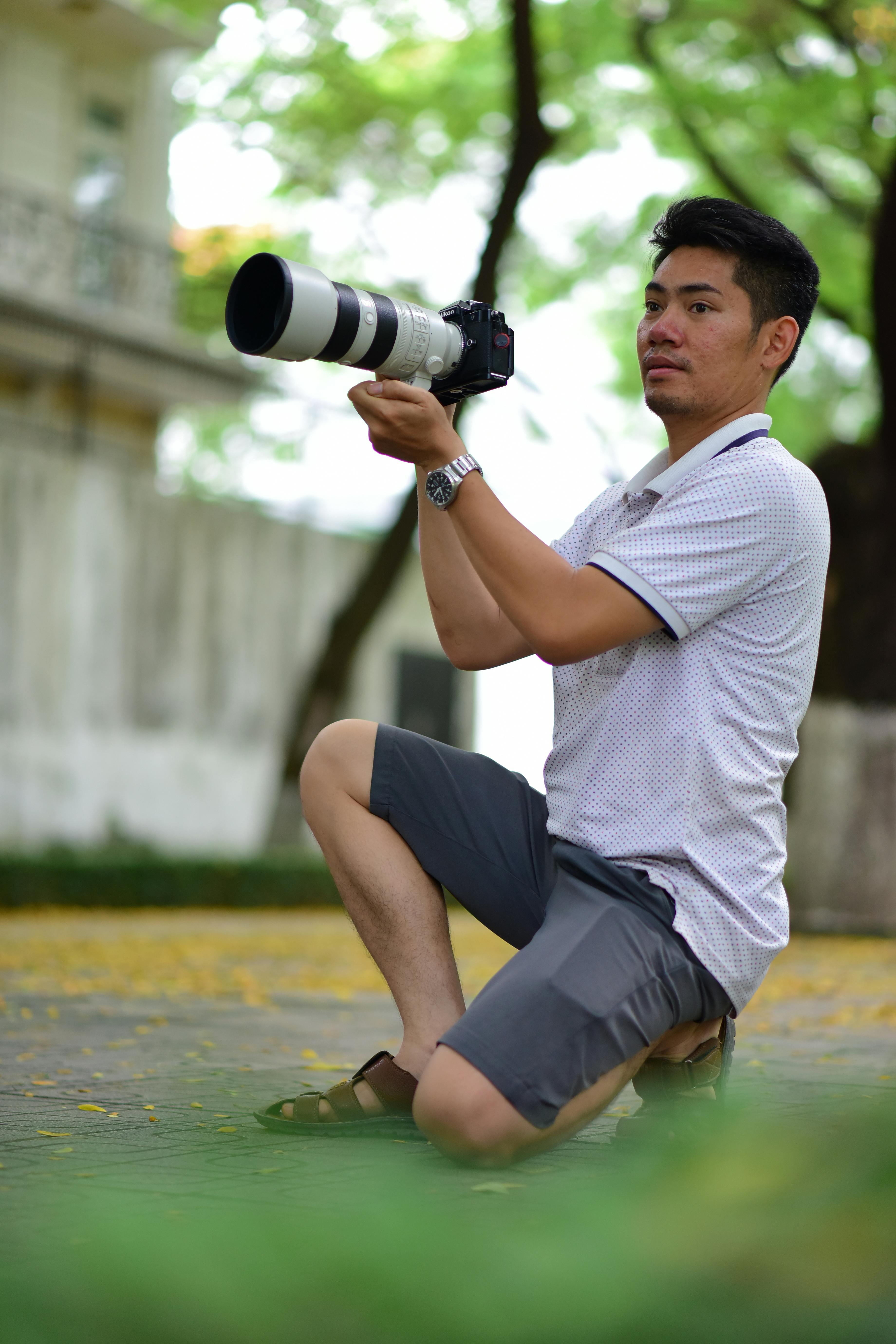 Photographer kneeling with a telephoto lens in a park setting, capturing nature.