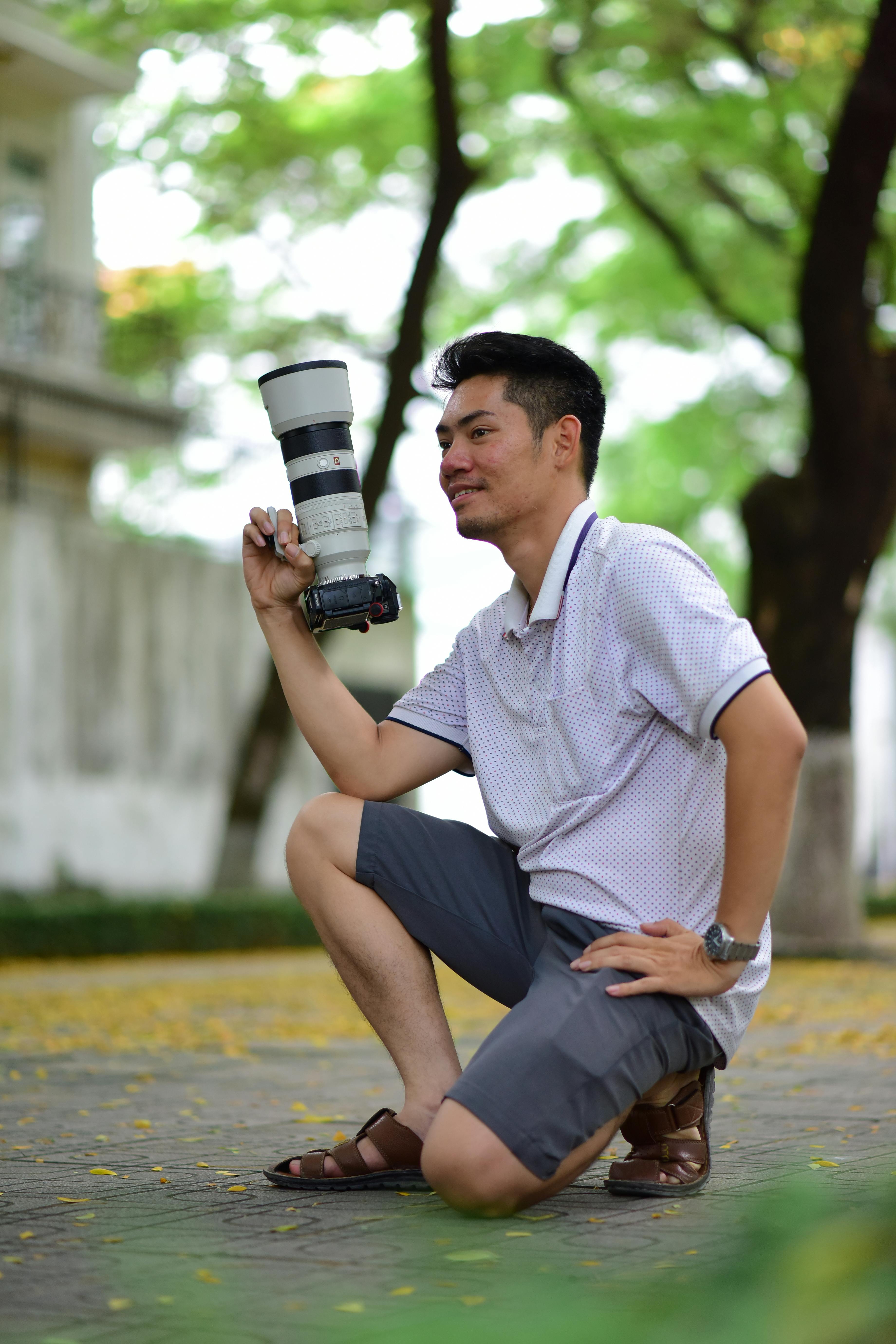 Photographer kneeling outdoors with telephoto lens on a sunny day.