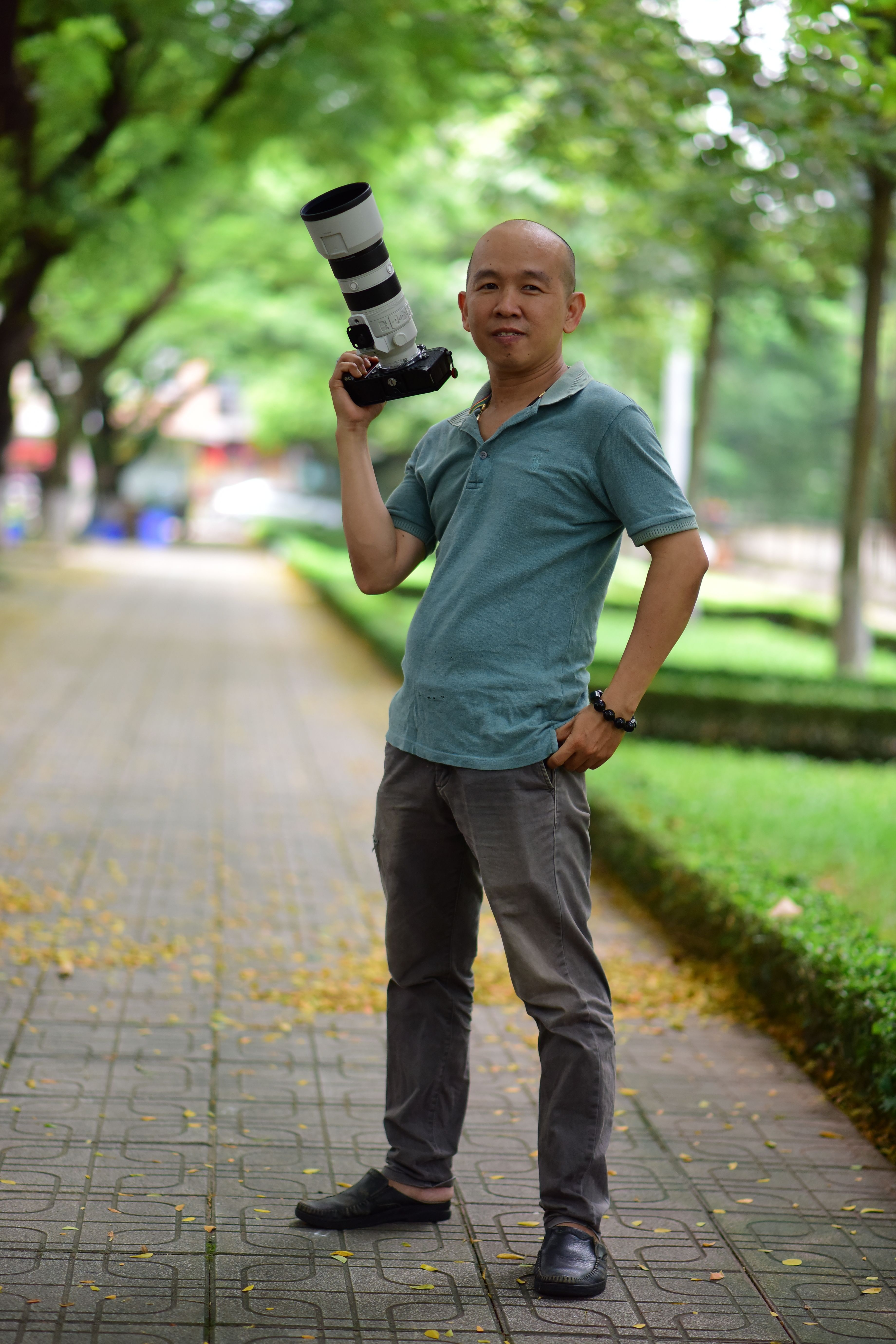 Outdoor portrait of a confident photographer holding a camera with a telephoto lens in a park setting.