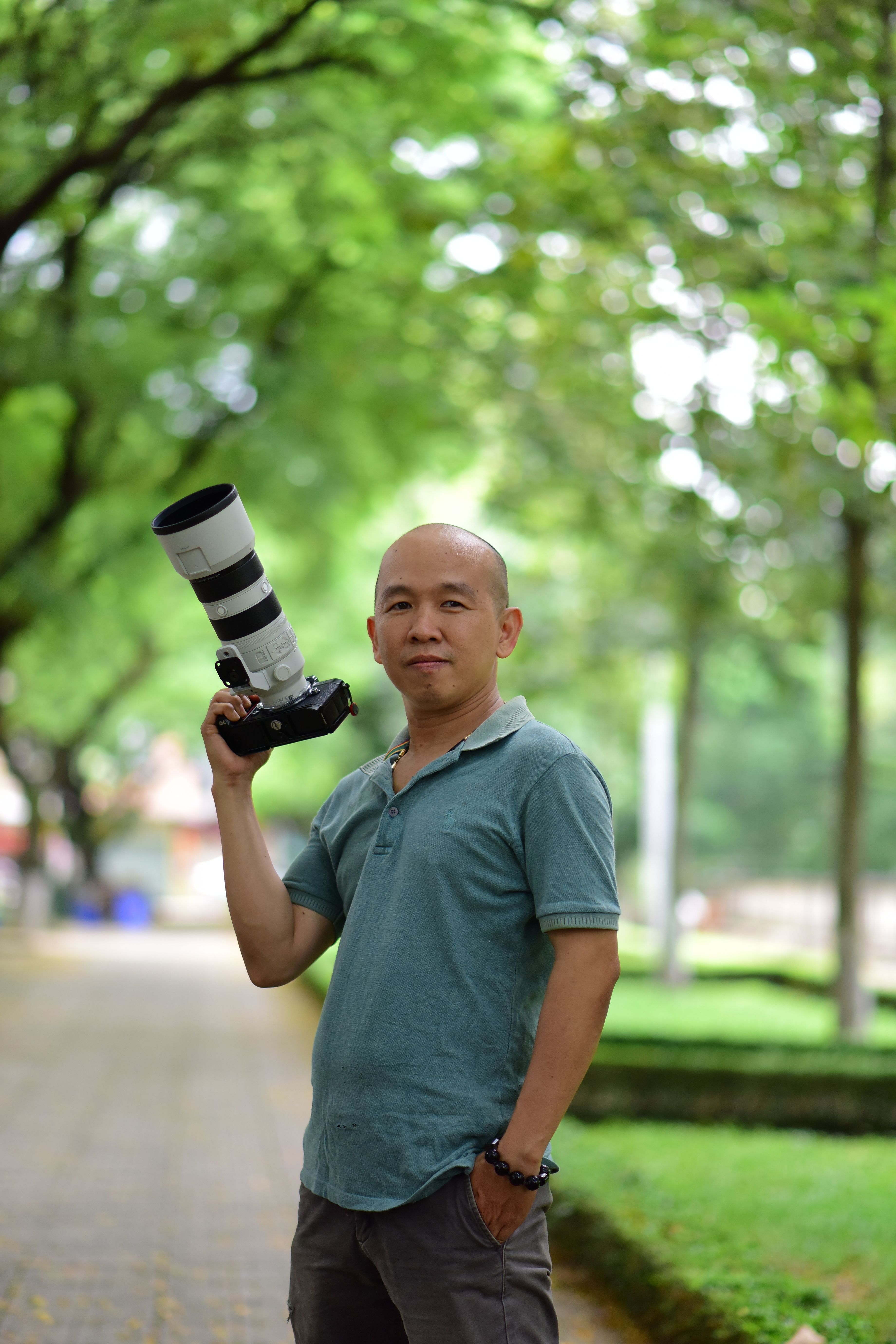 A male photographer outdoors holding a professional DSLR camera with telephoto lens.