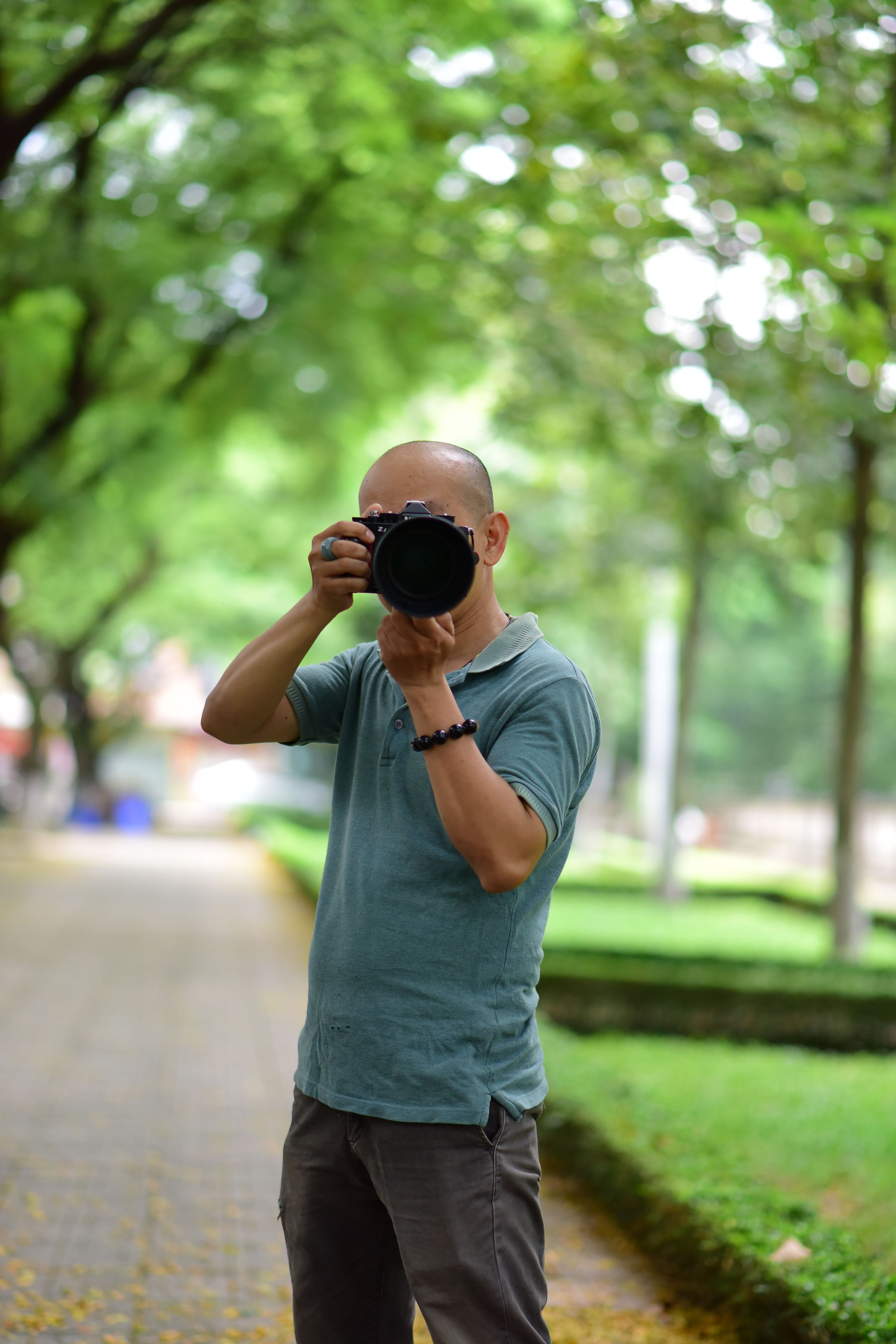 A man photographing in a lush green park, showcasing nature in a casual, outdoor setting.