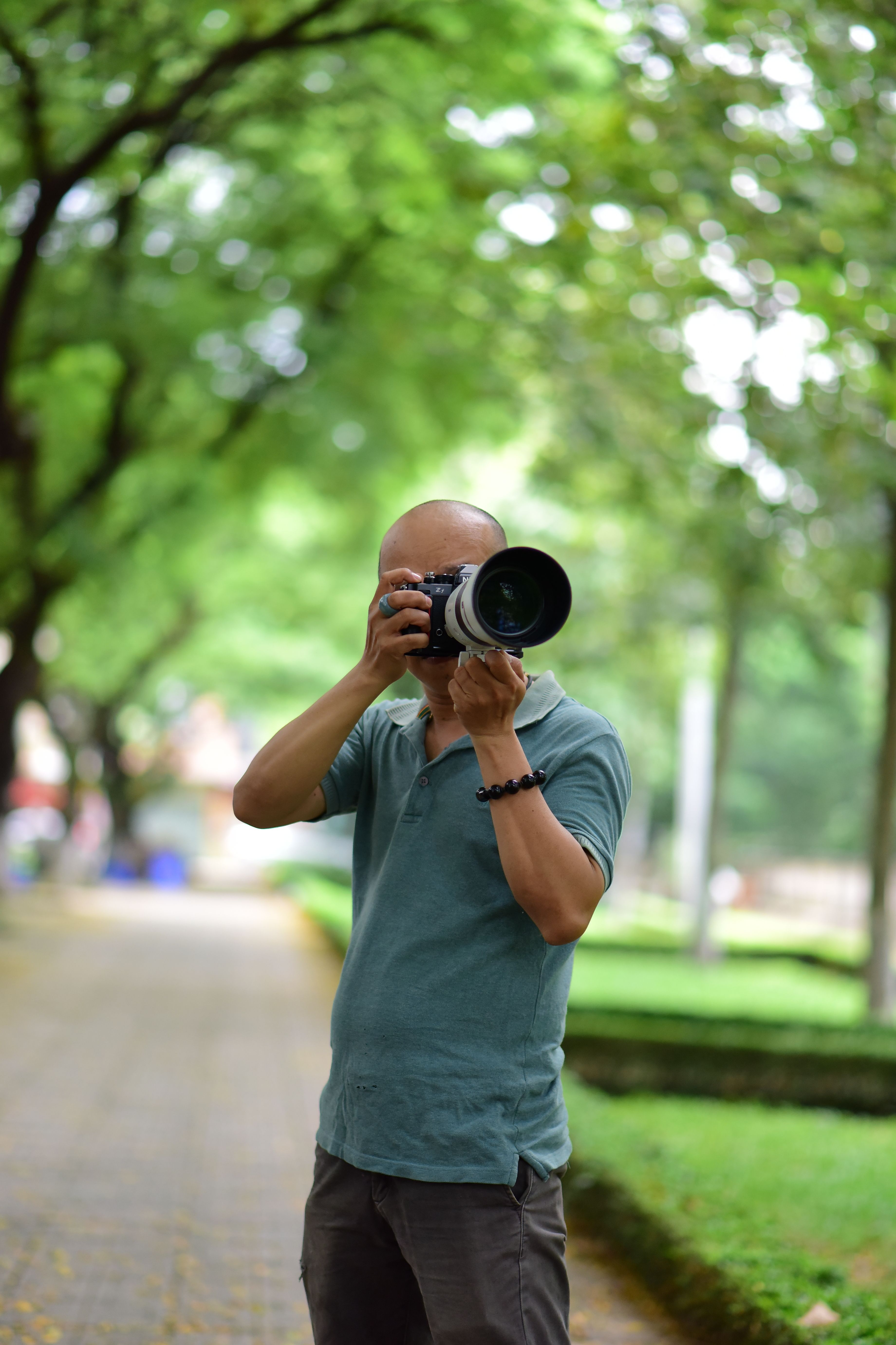 A man taking photos outdoors in a lush, green park setting with a DSLR camera.