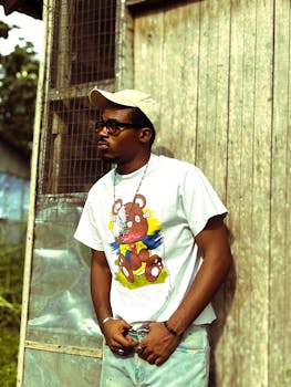 Young man in casual outfit with printed t-shirt, cap, and sunglasses outdoors.