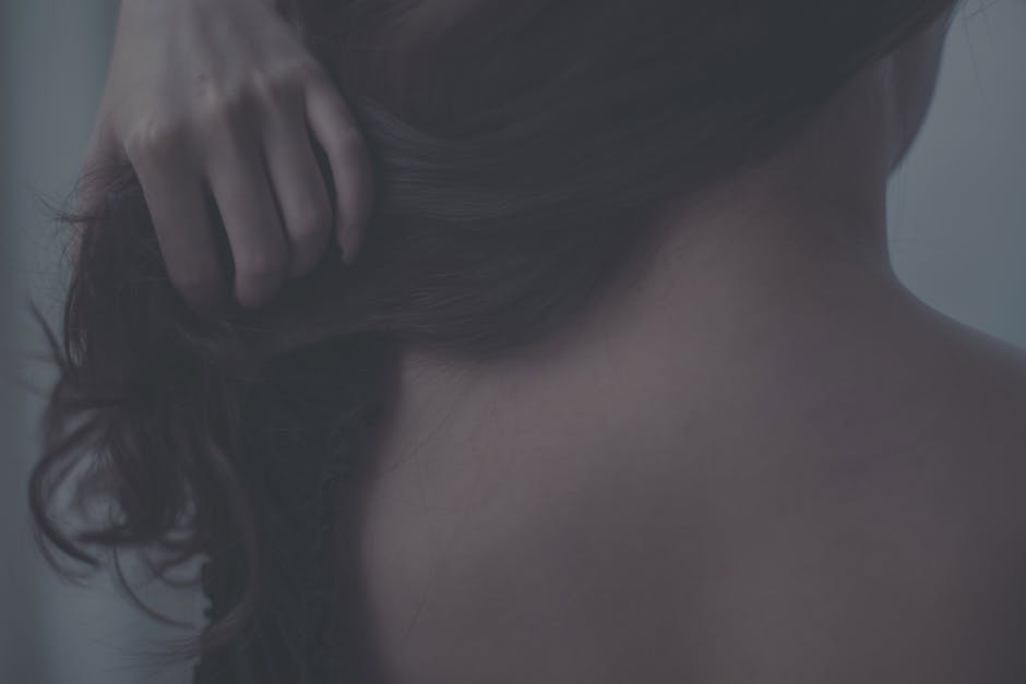 Artistic close-up of a woman gently touching her hair, capturing soft textures and intimate mood.