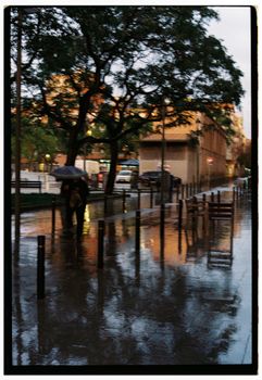 Moody urban street scene with rain and reflections under umbrellas.